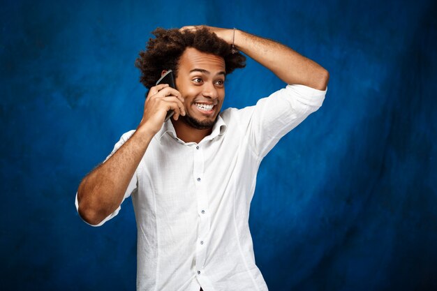 Hombre guapo joven hablando por teléfono sobre superficie azul