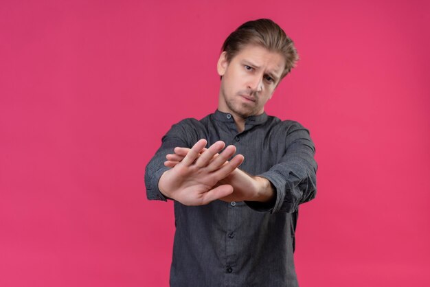 Foto gratuita hombre guapo joven haciendo gesto de parada con las manos frunciendo el ceño de pie sobre la pared rosa