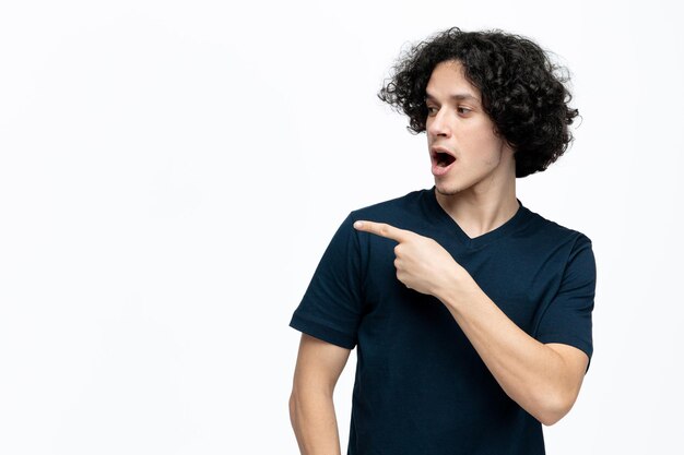 Hombre guapo joven impresionado mirando y señalando al lado aislado sobre fondo blanco con espacio de copia