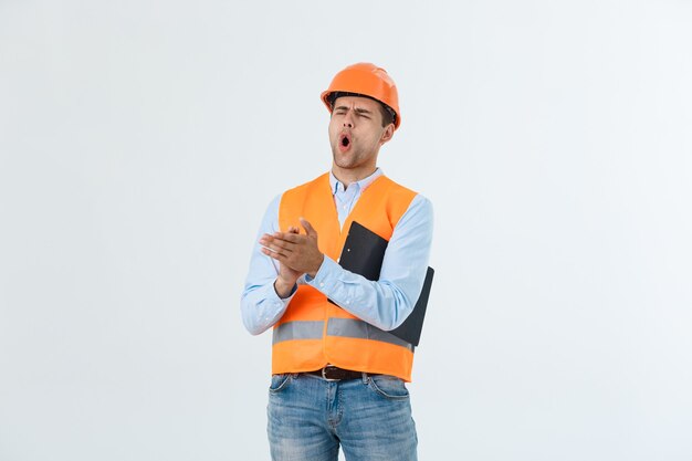 Hombre guapo joven ingeniero sobre gris con casco de seguridad con cara de sorpresa conmocionada.