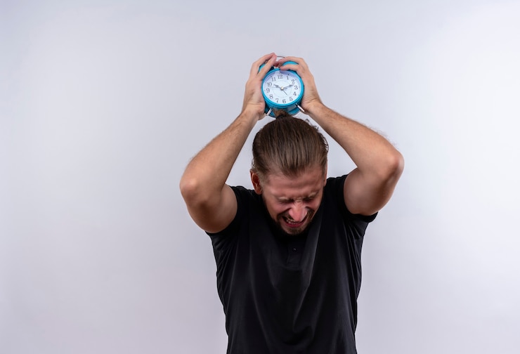 Foto gratuito hombre guapo joven molesto en camisa de polo negra que sostiene el reloj de alarma que va a tirar y romperlo de pie sobre fondo blanco