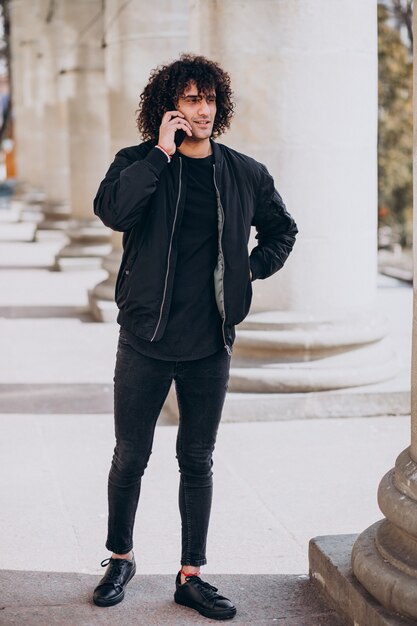 Hombre guapo joven con pelo rizado hablando por teléfono