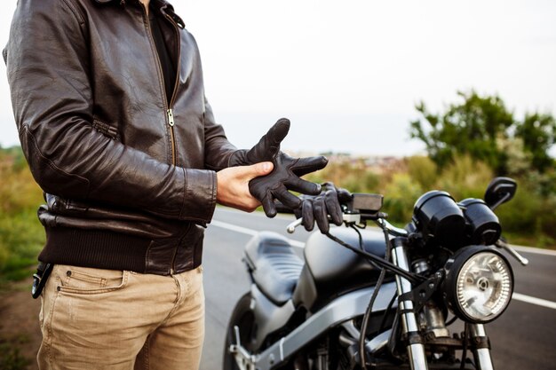 Hombre guapo joven posando cerca de su moto, con guantes.