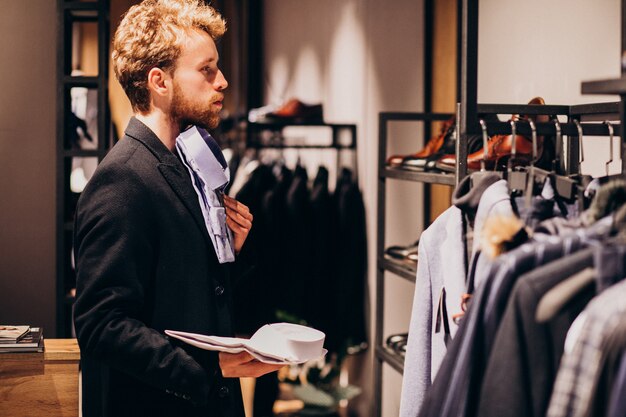 Hombre guapo joven que elige la camisa en una tienda