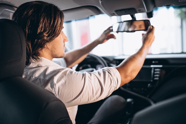 Hombre guapo joven que elige un coche en una sala de exposición de automóviles