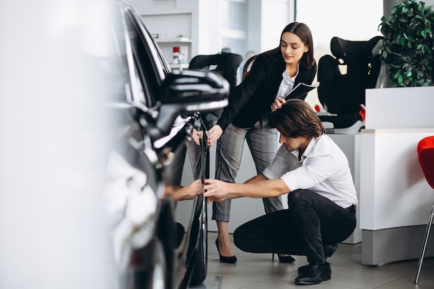 Hombre guapo joven que elige un coche en una sala de exposición de automóviles