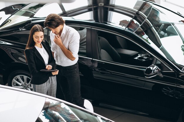 Hombre guapo joven que elige un coche en una sala de exposición de automóviles