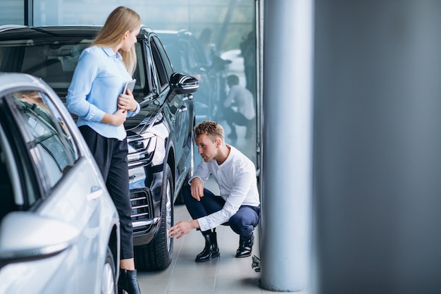 Hombre guapo joven que elige un coche en una sala de exposición de automóviles