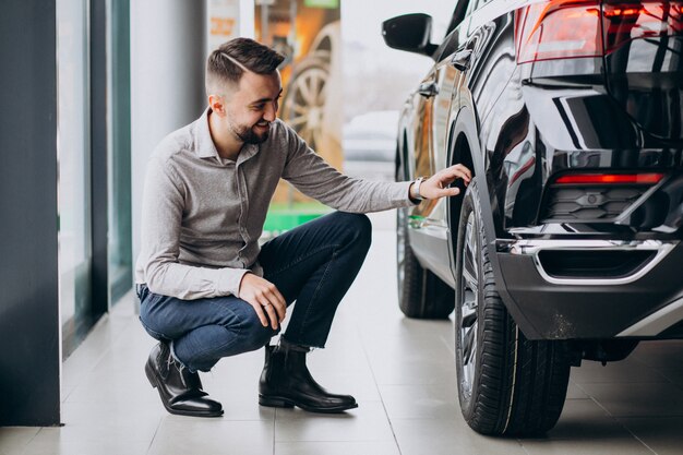 Hombre guapo joven que elige un coche en una sala de exposición de automóviles