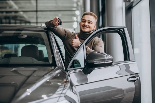 Hombre guapo joven que elige un coche en una sala de exposición de automóviles