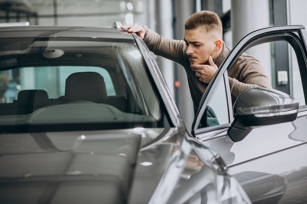 Hombre guapo joven que elige un coche en una sala de exposición de automóviles