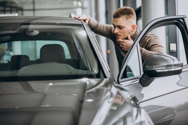 Hombre guapo joven que elige un coche en una sala de exposición de automóviles