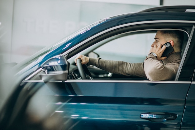 Hombre guapo joven que elige un coche en una sala de exposición de automóviles