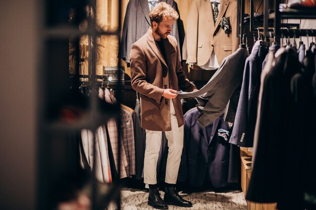 Hombre guapo joven que elige la ropa en la tienda