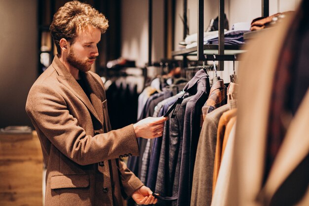 Hombre guapo joven que elige la ropa en la tienda