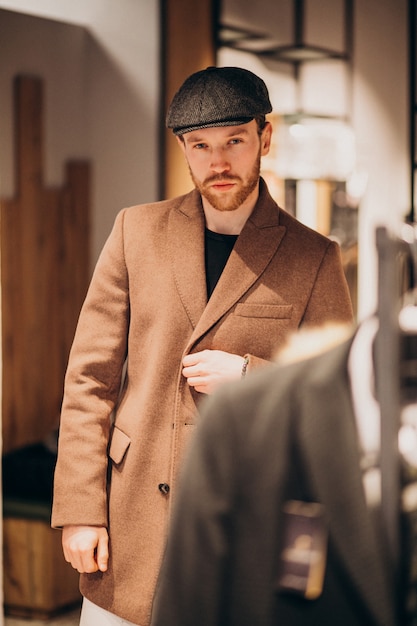 Hombre guapo joven que elige el sombrero en la tienda