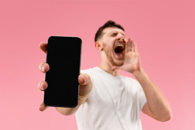 Hombre guapo joven que muestra la pantalla del teléfono inteligente aislada sobre fondo rosa en estado de shock con una sorpresa
