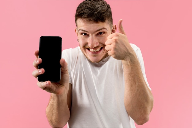 Hombre guapo joven que muestra la pantalla del teléfono inteligente en rosa con una cara de sorpresa