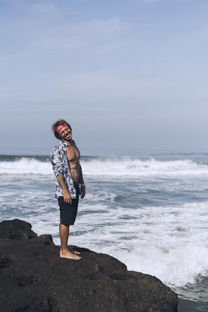 Hombre guapo joven en una roca junto al mar.