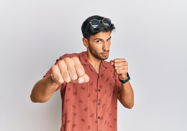 Hombre guapo joven con ropa informal de verano golpeando el puño para luchar contra la amenaza y la violencia de ataques agresivos y enojados