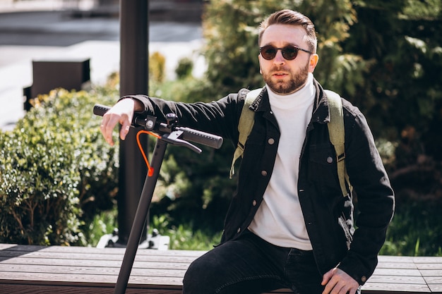 Foto gratuita hombre guapo joven sentado con scooter en el parque