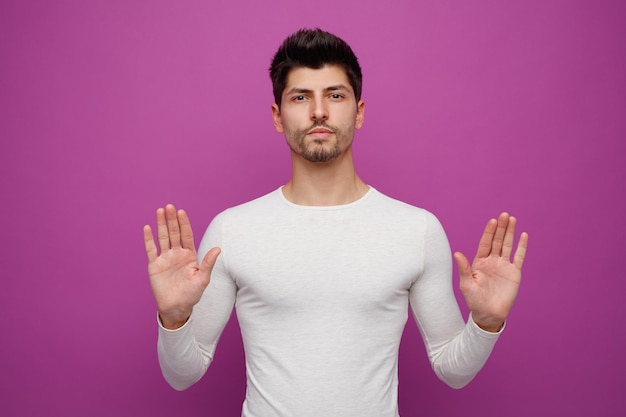 Hombre guapo joven serio mirando a la cámara mostrando las manos vacías sobre fondo púrpura