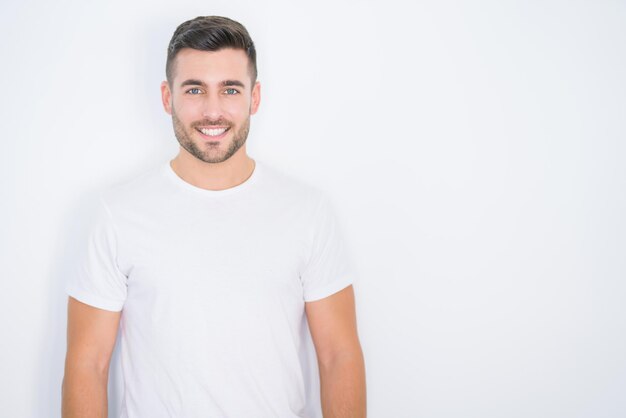Hombre guapo joven sonriendo feliz vistiendo camiseta blanca casual sobre fondo blanco aislado
