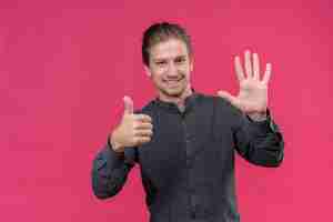 Foto gratuita hombre guapo joven sonriendo mostrando y apuntando hacia arriba con los dedos número seis de pie sobre la pared rosa