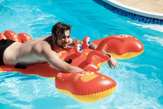 Hombre guapo joven sonriendo, nadando en el cangrejo de aire en la piscina