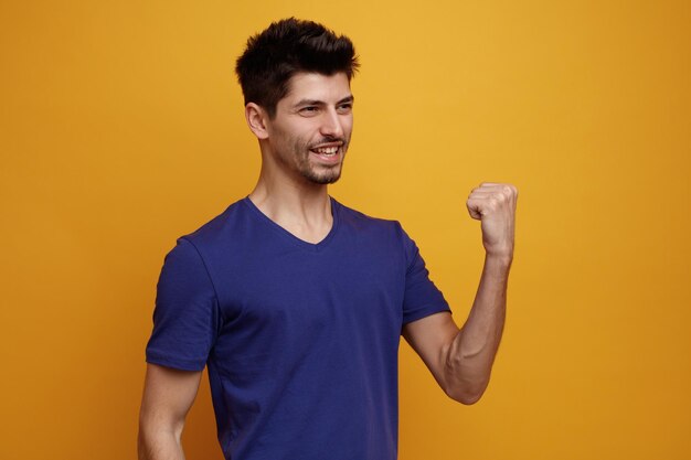 Hombre guapo joven sonriente mirando al lado sosteniendo el puño en el aire sobre fondo amarillo