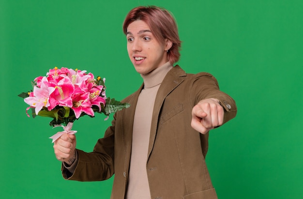 Hombre guapo joven sorprendido sosteniendo y mirando el ramo de flores apuntando hacia adelante