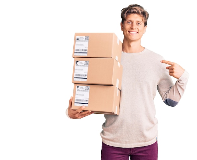 Foto gratuita hombre guapo joven sosteniendo el paquete de entrega apuntándose con el dedo a uno mismo sonriendo feliz y orgulloso