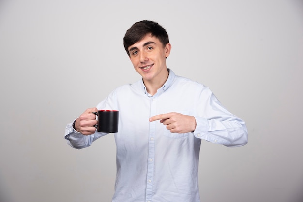 Hombre guapo joven sosteniendo una taza de té en la pared gris.