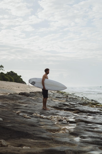 Hombre guapo joven con una tabla de surf en el océano.