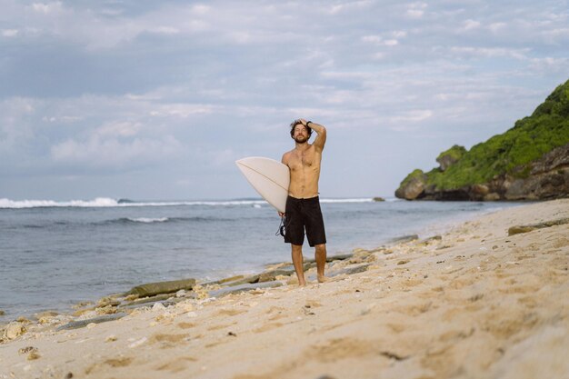 Hombre guapo joven con una tabla de surf en el océano.