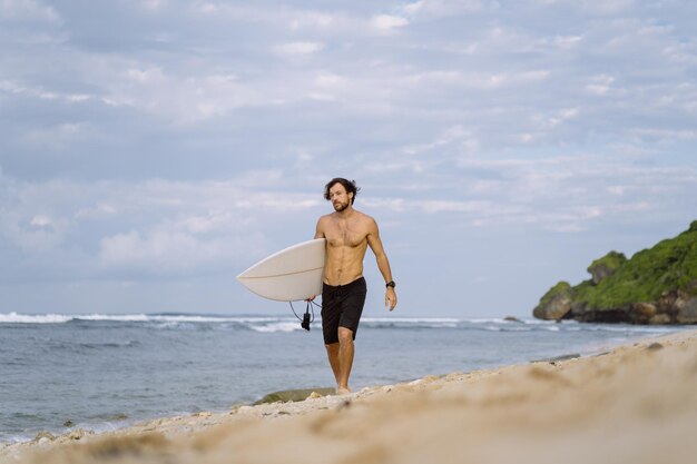 Hombre guapo joven con una tabla de surf en el océano.