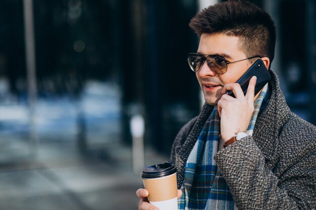 Hombre guapo joven tomando café fuera y usando el teléfono