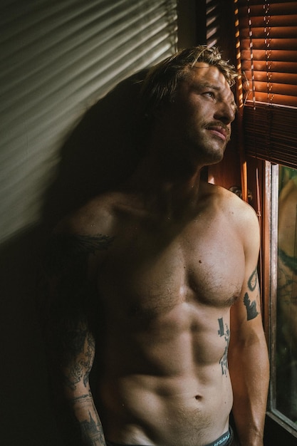 Hombre guapo joven con un torso desnudo en tatuajes. Retrato, luz artística.