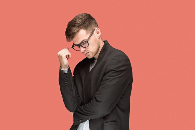 Hombre guapo joven en traje negro y gafas aislado en la pared roja