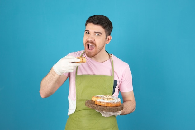 Hombre guapo joven tratando de morder la rebanada de pastel en un azul.