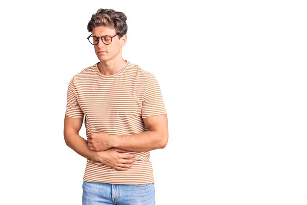 Hombre guapo joven vestido con ropa informal y gafas con la mano en el estómago porque la indigestión dolorosa enfermedad sensación malestar dolor concepto