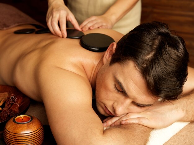 Hombre guapo con masaje con piedras en el salón de spa. Estilo de vida saludable.