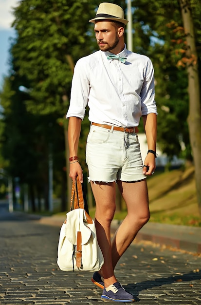 Hombre guapo modelo hipster en ropa de verano elegante posando en sombrero con bolsa