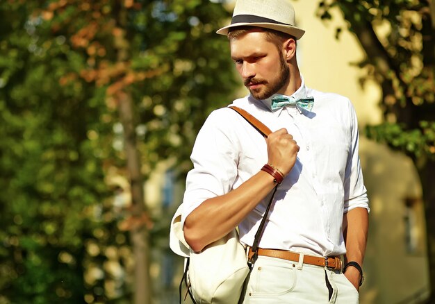 Hombre guapo modelo hipster en ropa de verano elegante posando en sombrero con bolsa