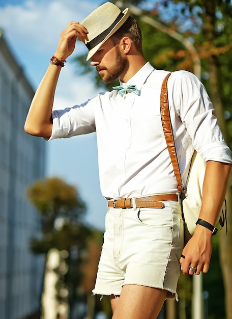 Hombre guapo modelo hipster en ropa de verano elegante posando en sombrero con bolsa