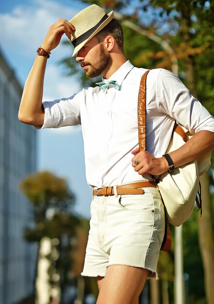 Hombre guapo modelo hipster en ropa de verano elegante posando en sombrero con bolsa