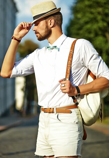 Hombre guapo modelo hipster en ropa de verano elegante posando en sombrero con bolsa