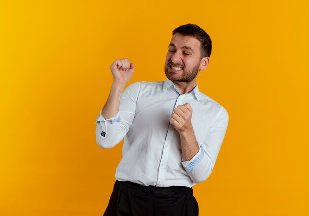 Hombre guapo molesto se encuentra con los puños levantados aislados en la pared naranja