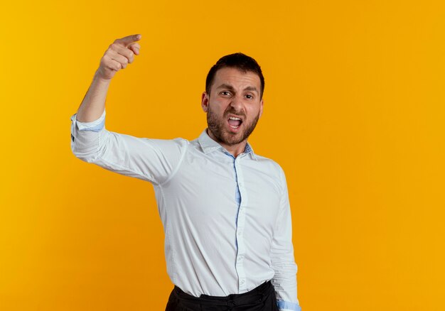 Hombre guapo molesto le grita a alguien que apunta hacia adelante aislado en la pared naranja