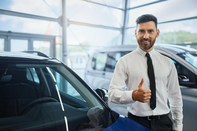 Hombre guapo mostrando el pulgar hacia arriba mientras compra un coche en el salón